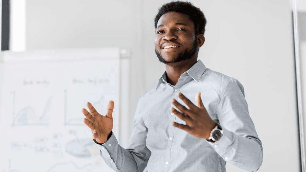 Person presenting with charts behind them. 