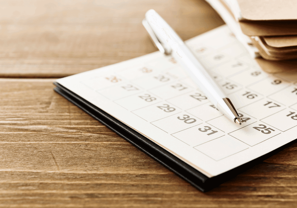 Calendar and pen resting on wood table.