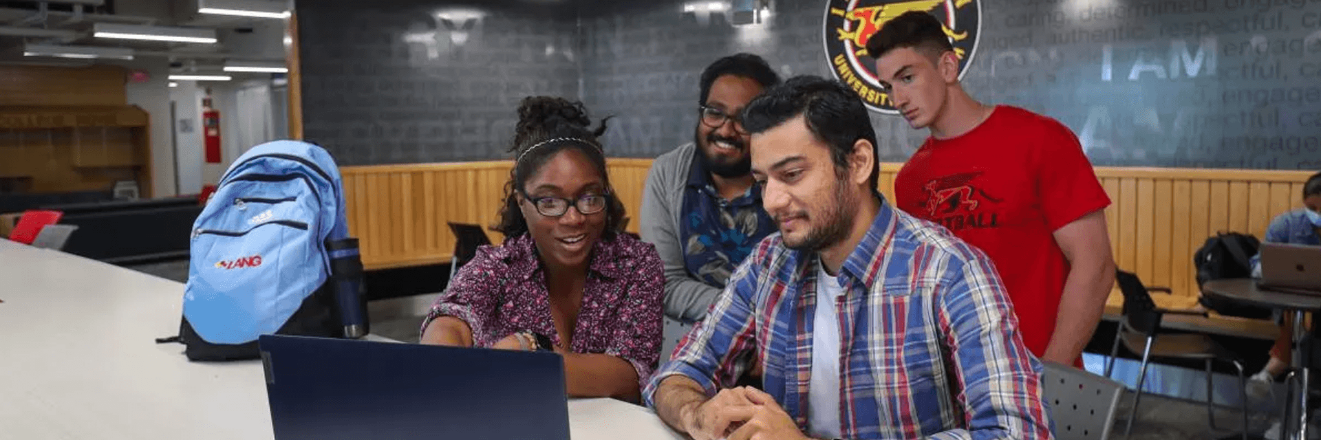 a photo of students point and looking at a laptop