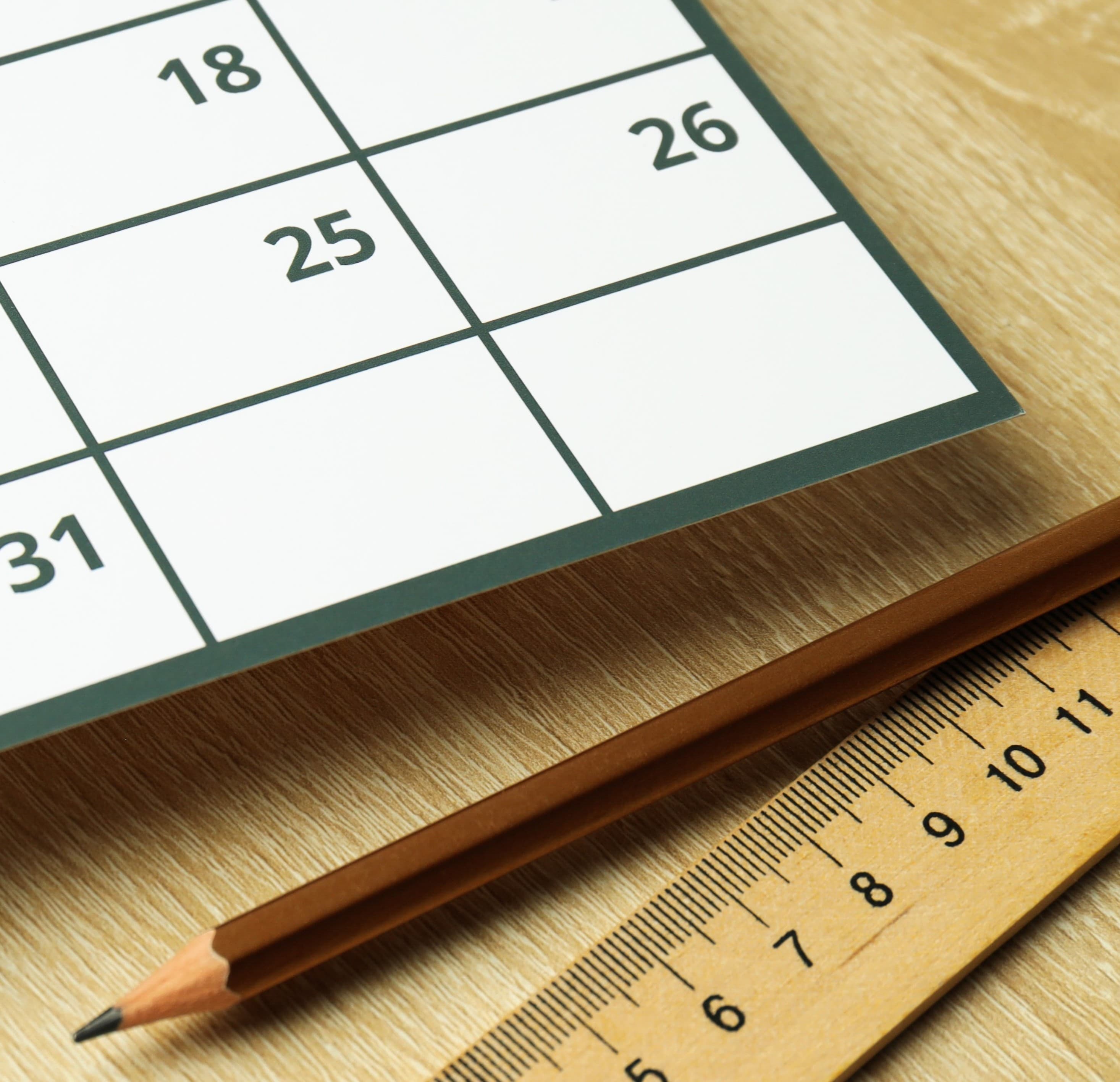 A calendar laying on a desk beside a pencil and ruler.